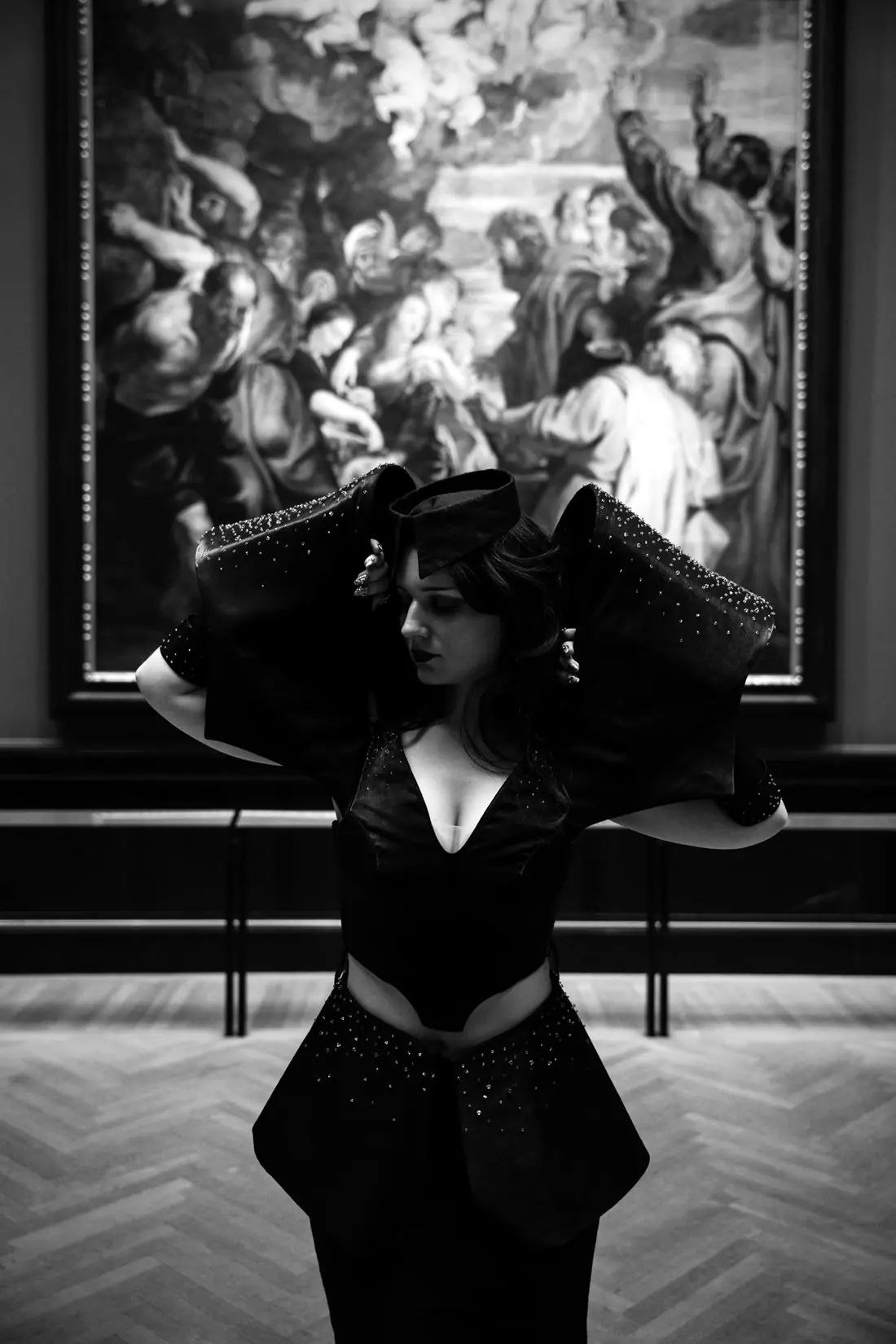 Hands raised to the headpiece in front of a baroque painting.